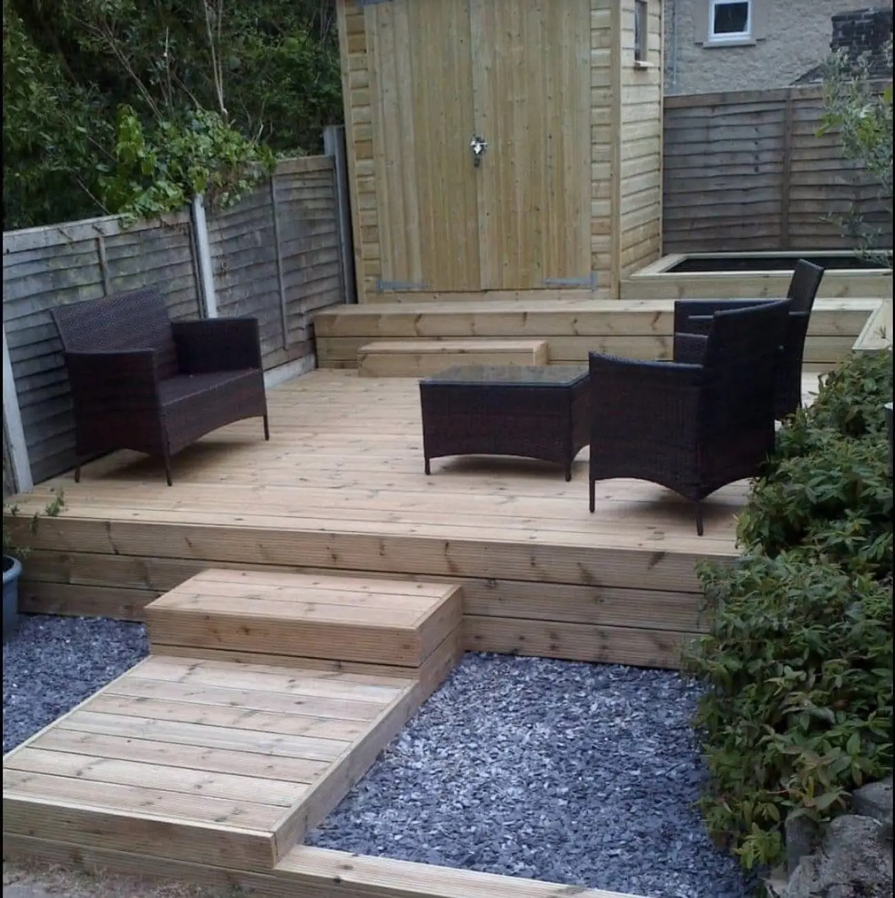 Raised timber deck with rattan chairs and table, sleeper steps and slate gravel borders