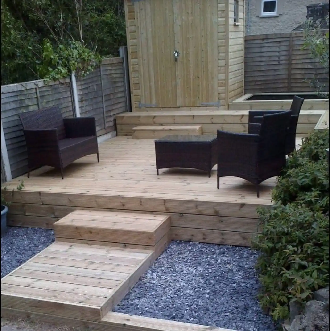 Raised timber deck with rattan chairs and table, sleeper steps and slate gravel borders