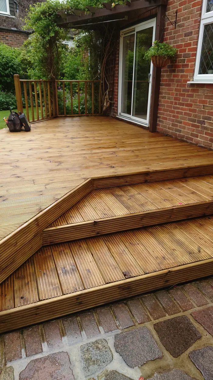 Timber deck with wide corner steps leading down to a cobbled path beside a house