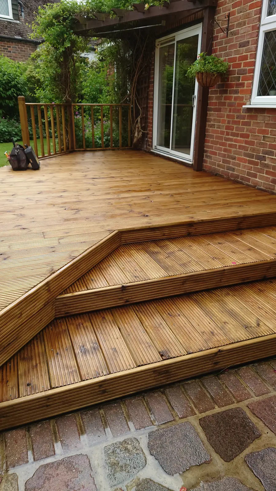 Timber deck with wide corner steps leading down to a cobbled path beside a house