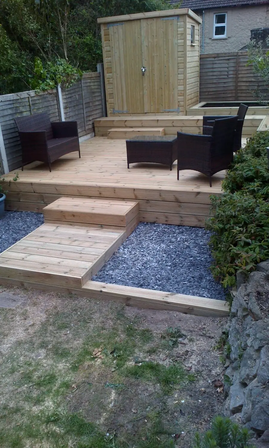 Raised timber deck with rattan seating, wide sleeper steps and a garden store, edged in slate gravel