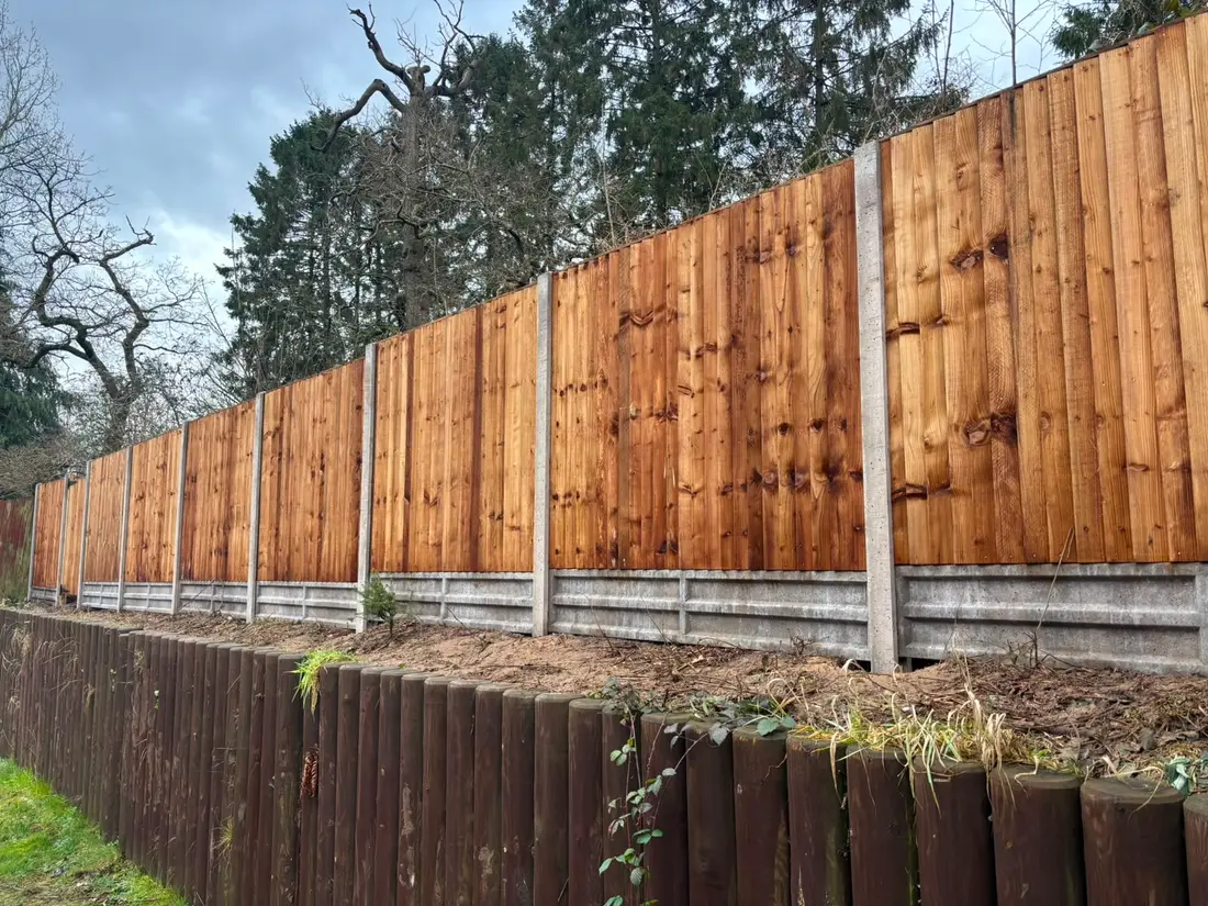 A long run of new closeboard fence panels on concrete posts and gravel boards, above a log roll retaining edge