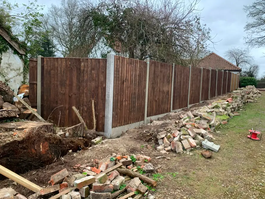 A dark stained closeboard fence replacing an old boundary, with cleared stumps and reclaimed brick alongside
