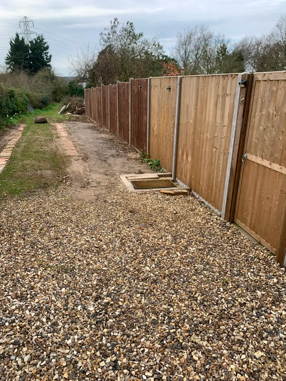 A new fence line running the length of a gravelled side path with a matching timber gate