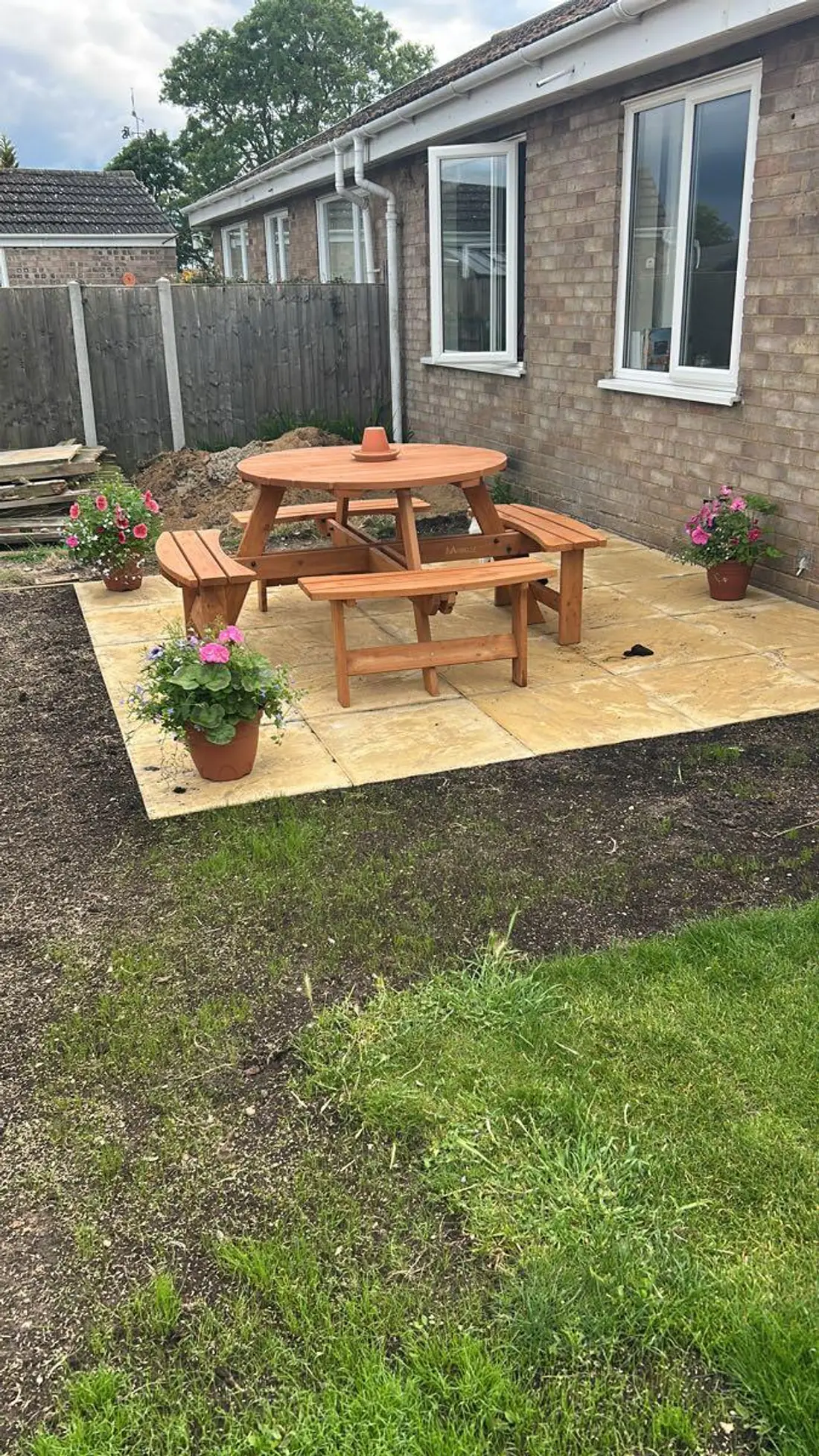 A finished paving slab patio with a wooden picnic bench and potted flowers outside a Norwich bungalow