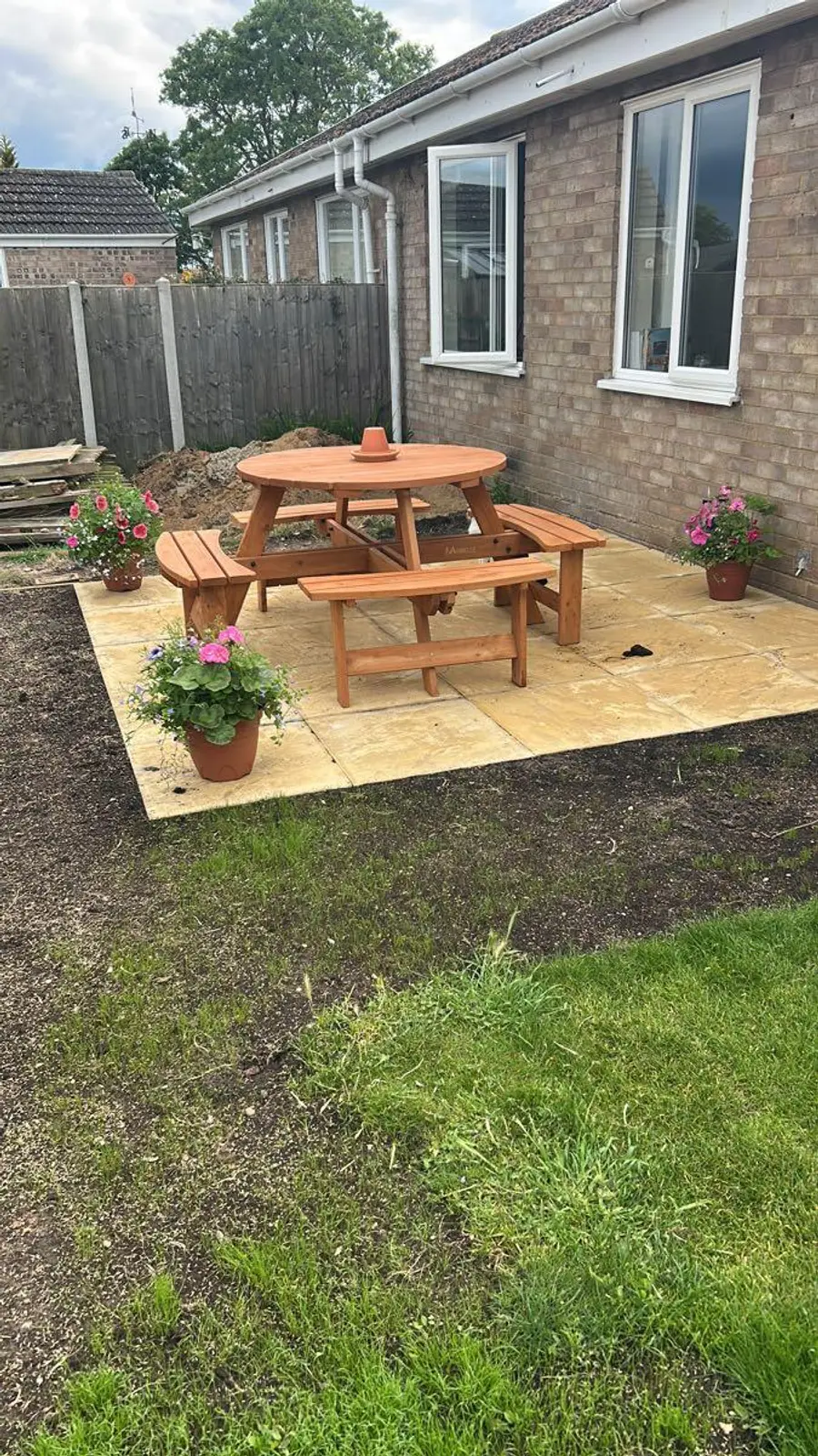 A finished paving slab patio with a wooden picnic bench and potted flowers outside a Norwich bungalow